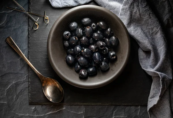 Top down view of a black bowl filled with black olives against a dark background. — Stock Photo, Image