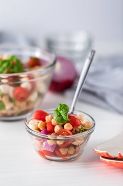 Fesleğenle süslenmiş, yemeye hazır küçük bir kase garbanzo fasulyesi salatası..