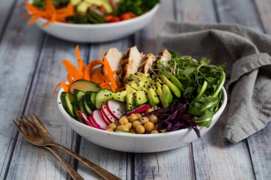 A top down close up view of a buddha bowl filled with various vegetables and grilled chicken. Healthy eating concept.