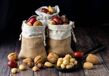 A close up of three burlap sacks filled with assorted nuts in the shell against a dark background.