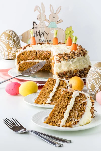 Two slices of carrot cake with the cake in behind and surrounded by Easter decorations.
