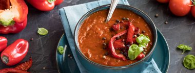 Kavrulmuş kırmızı biber ve fesleğenle süslenmiş bir kase kırmızı biber çorbası..