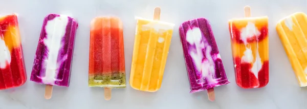 A top down view of a row of various homemade fresh fruit popsicles against a marble background. — Stock Photo, Image