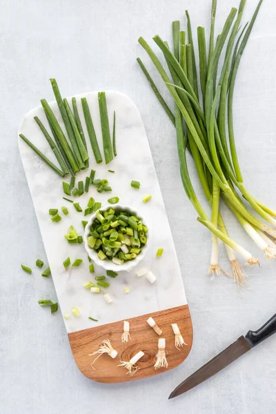 Mermer kesim tahtasının üzerinde doğranmış yeşil soğanın yukarıdan görünüşü. 