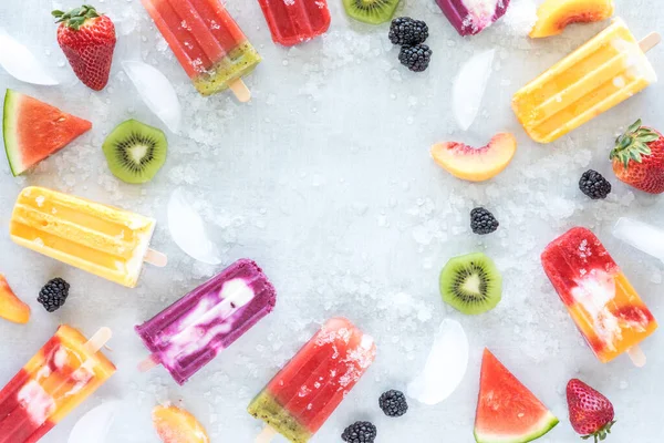 Flat lay of various homemade fruit popsicles as well as pieces of cut and whole fruit. — Stock Photo, Image