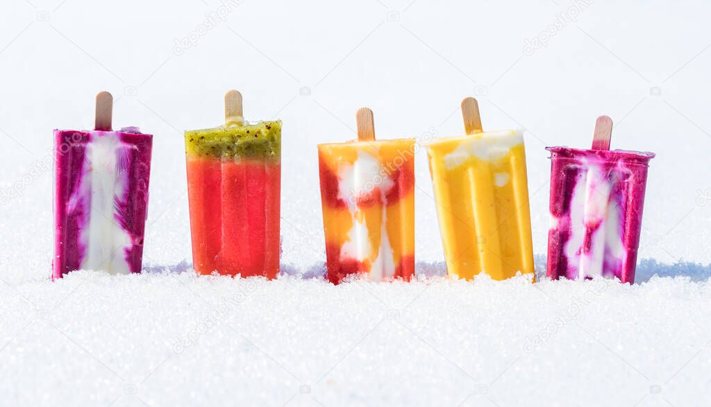 A close up front view of a row of upside down popsicles in snow against a white background.