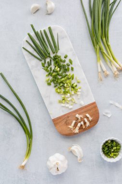 Yeşil soğan ve sarımsak ile çevrili mermer kesme tahtasının üzerinde doğranmış yeşil soğanın yukarıdan görünüşü. 
