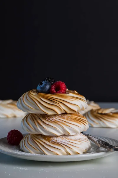 Een close-up van drie meringues in een stapel met bessen bovenop, tegen een zwarte achtergrond. — Stockfoto