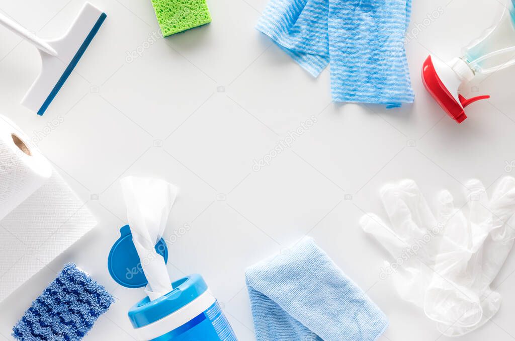 Top down view of a variety of house cleaning supplies against a white background.