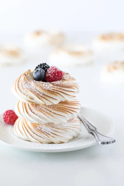 A stack of toasted meringues and berries against a white background with other meringues in soft focus in behind. — Stock Photo, Image
