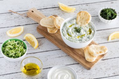 Tzatziki sosunun yukarıdan görünüşü, sosu ve pideleri yapmak için kullanılan malzemelerle çevrili..