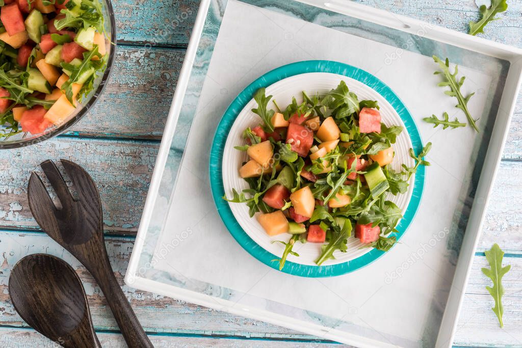 A top down view of a dish filled with watermelon and arugula salad ready for eating.