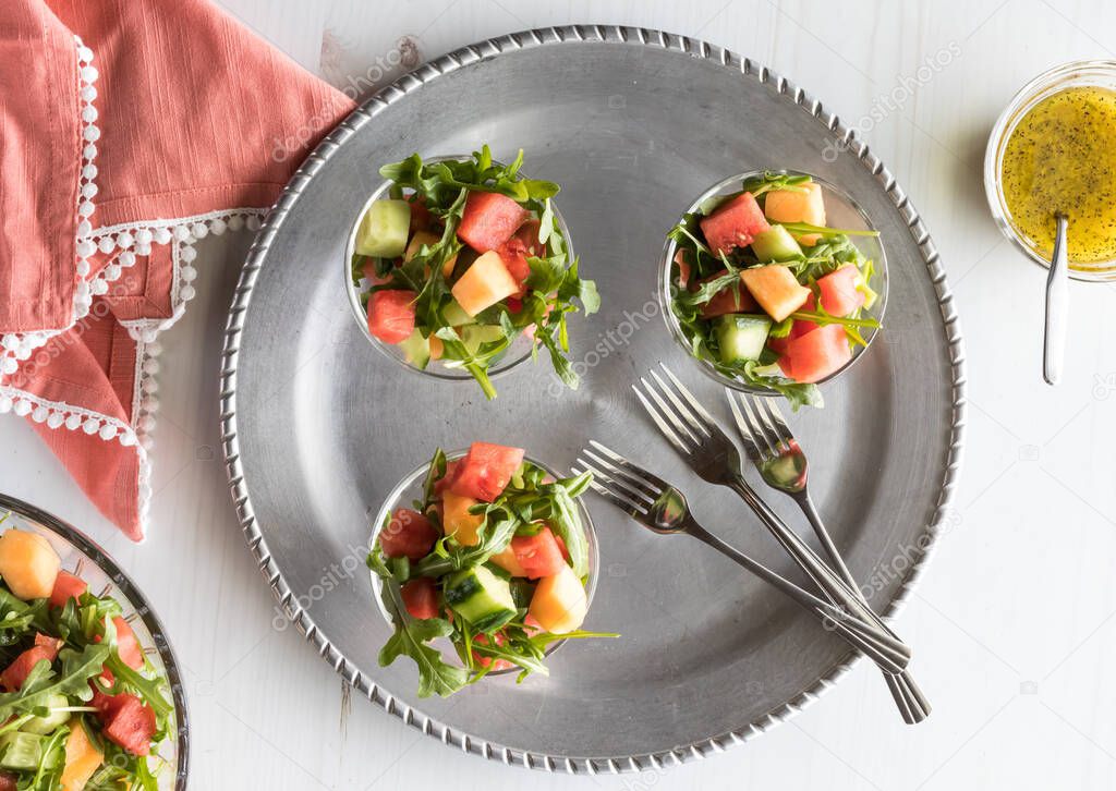 A top down view of a metal tray with three servings of watermelon and arugula salad.