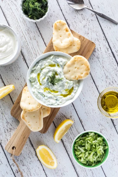 Tzatziki 'nin yukarıdan aşağı dikey görüntüsü ahşap bir tahtanın üzerinde, atıştırmalık olarak pide ısırıklarla servis ediliyor..