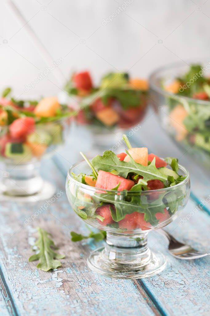 A close up view of a serving of watermelon arugula salad with more salads in behind.
