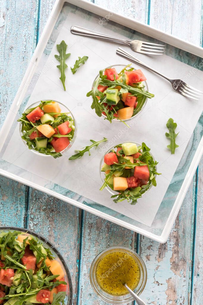 A top down view of three servings of watermelon and arugula salad in a serving tray.