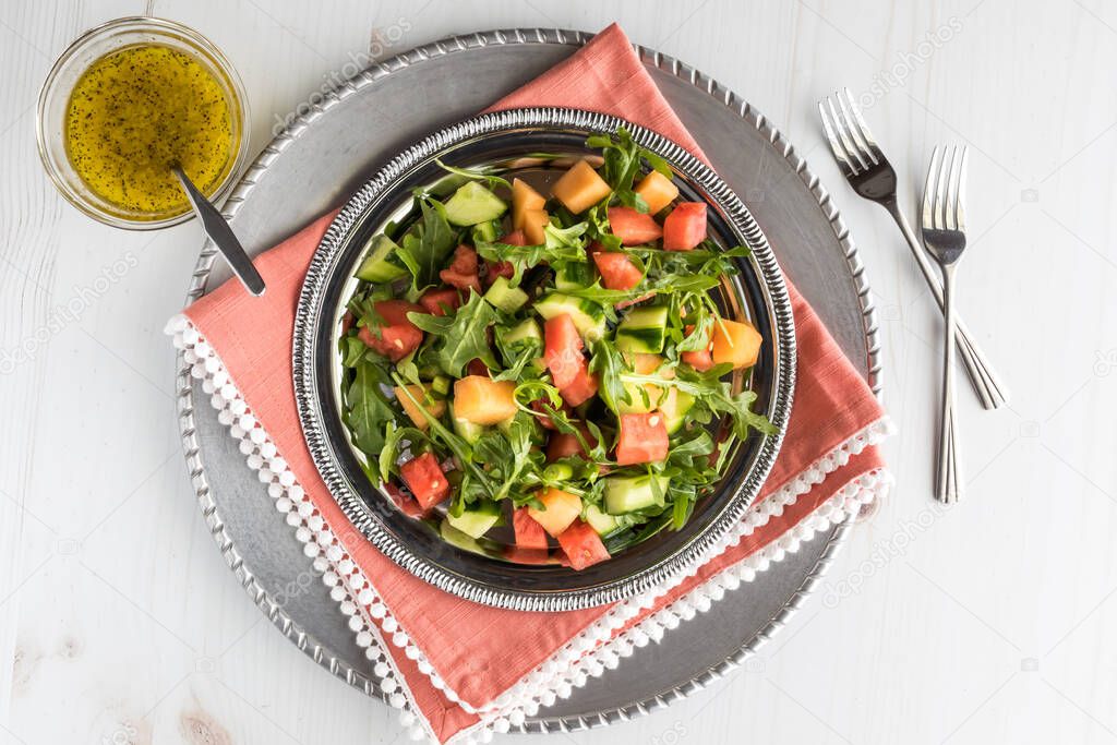 A top down view of watermelon and arugula salad with dressing.