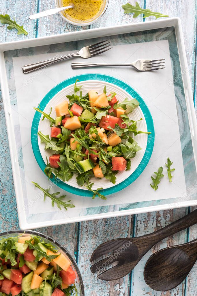 A top down vertical view of a plate of watermelon and arugula salad on a serving tray.