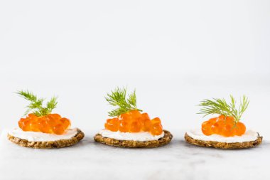 Kırmızı havyarla kaplanmış ve dereotuyla süslenmiş kraker ve krem peynir kanepelerinin yakın çekim görüntüsü..