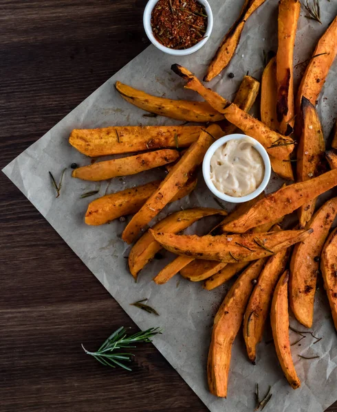 Una vista de arriba hacia abajo de papas fritas en papel pergamino sobre una mesa de madera lista para comer . — Foto de Stock