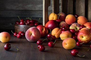 Koyu arkaplana karşı ahşap bir sandıktan taştan meyvelerin döküldüğü bir cephe..