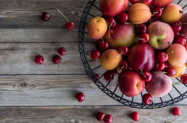 Taş meyve ve kirazlarla dolu bir metal kasenin yukarıdan görünüşü ahşap bir masaya dökülüyor ve uzayı kopyalıyor..