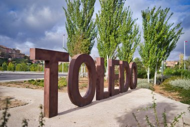 İspanya, Toledo 'ya hoş geldiniz. Toledo şehrinin girişindeki hoş geldin tabelasında yerde büyük harfler ve kahverengi harfler var. Arka planda bulutlu güneşli bir günde eski şehir.