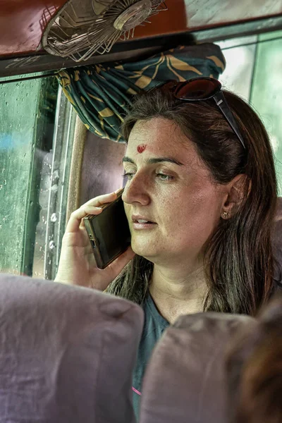 Западная туристка с красной точкой на лбу (бинди) в местном автобусе Катманду разговаривает по телефону — стоковое фото