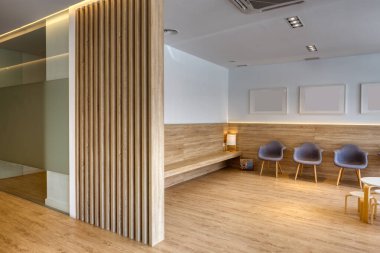 Gri sandalyeli, resimli, beyaz duvarlı modern tasarım resepsiyonu. Ahşap zemin ve ekran. Diş Kliniği.