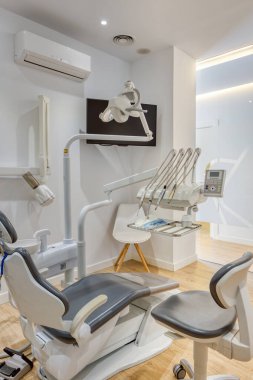 Tam donanımlı, beyaz duvarları ve ahşap zemini olan modern diş kliniği kutusu. Monitörde diş radyografisi gösteriliyor.