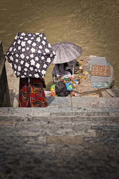 Kvinna med paraply och lång kjol går ner för trapporna så att siaren bredvid den bruna floden kommer att läsa framtiden i en ghat av Pashupatinath krematorium i Katmandu. Resebegrepp. — Stockfoto