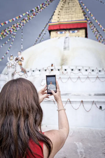 Close-up of brown hair wesrtern gilr taking photos with his smartphone to the Boudhanath's stupa in Kathmandu. Woman from behind. bokeh — ストック写真