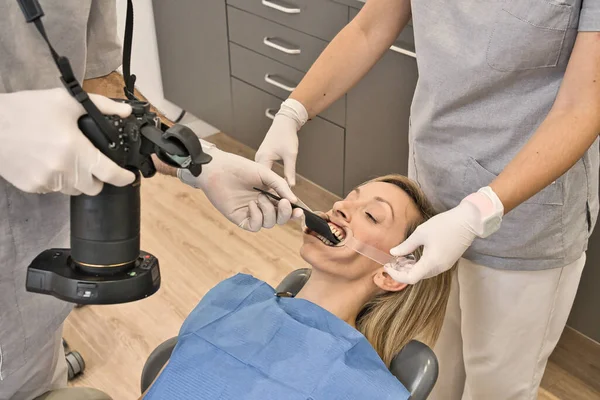 Zahnarzt mit blauer Maske überprüft den Gesundheitszustand seiner Patientin, die im Sessel einer modernen Zahnklinik liegt. Fotografieren mit einem Reflex die Zähne des Patienten. Makrofotografie — Stockfoto