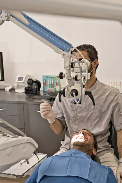 Dental doctor with microscope and hygienic gloves checking the dental health of his patient in a modern clinic — Stock Photo, Image