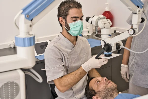Dental doctor with microscope and hygienic gloves checking the dental health of his patient in a modern clinic — Stock Photo, Image