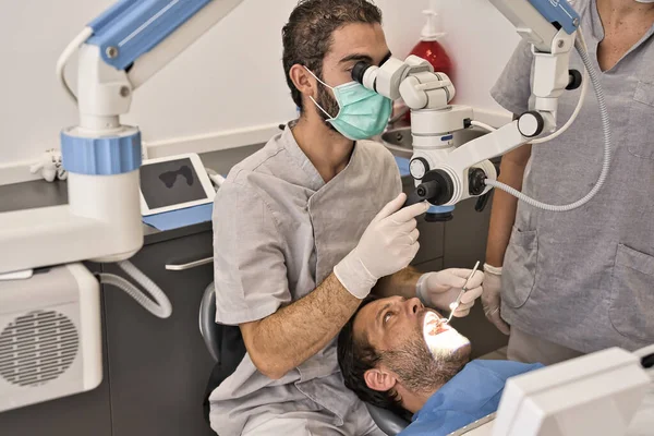 Médico dentário com microscópio e luvas higiênicas verificando a saúde dental de seu paciente em uma clínica moderna — Fotografia de Stock