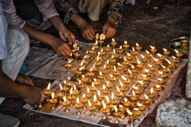 İnsanlar yerde çömelmiş tereyağı lambaları yakıyor. Dua etmek için yerel gazetelerin üzerine lambalar dökülüyor. Nepal, Asya