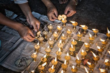 İnsanlar yerde çömelmiş tereyağı lambaları yakıyor. Dua etmek için yerel gazetelerin üzerine lambalar dökülüyor. Nepal, Asya