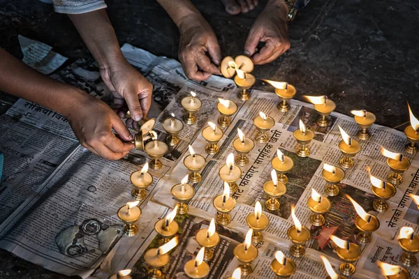 İnsanlar yerde çömelmiş tereyağı lambaları yakıyor. Dua etmek için yerel gazetelerin üzerine lambalar dökülüyor. Nepal, Asya