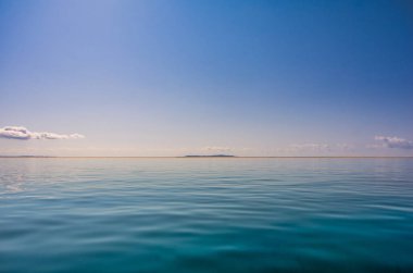 Tropikal deniz bulutlu, mavi gökyüzü ve deniz yosunlarının arka planını görebilen şeffaf bir gökyüzü. Ufuktaki ada profili, Tropikal deniz bulutlu mavi gökyüzü ve şeffaf