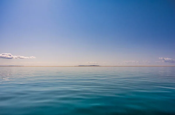 Tropical sea gentle blue sky with clouds and with transparent that allow to see the seaweed background. Island profile on the horizon,Tropical sea gentle blue sky with clouds and with transparent that