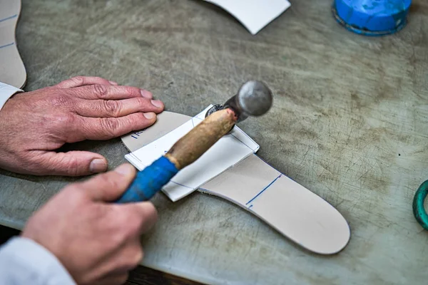 Hands of an orthopedic artisan sticking with the help of a mace some artisan and personalized foot templates.Hands of an orthopedic artisan sticking with the help of a blue wooden mallet some foam tem
