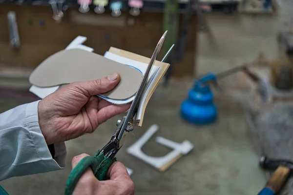 Ortopedik bir zanaatkarın elleri köpük şablonlar ve plastik işçilerle makas kesiyor ve ayakları için kişiselleştiriliyor. Çalışma tezgahının altında mavi yapıştırıcı var..