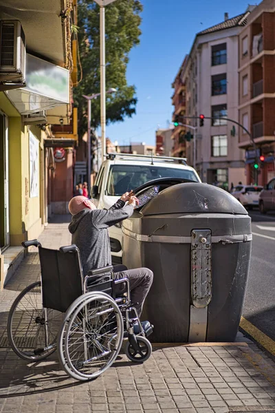 Rollstuhlfahrer nehmen eine durchsichtige Plastikflasche auf, die auf den Boden geworfen wird, um sie in den Recyclingcontainer zu werfen und sich nicht zu verunreinigen. Kunststoffe vermeiden — Stockfoto