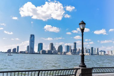 Güneşli bir günde Battery Park 'tan New Jersey silueti. Ağaçların ve sokak lambalarının arasından şehir manzarası. Şehir ve seyahat konsepti. Manhattan, New York City, Usa