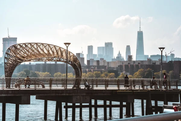 Pessoas a passear num cais de Brooklyn ao pôr-do-sol. No fundo Manhattan apartamento e edifícios de escritórios. Conceito de vida na cidade. Brooklyn, Nova Iorque, EUA — Fotografia de Stock