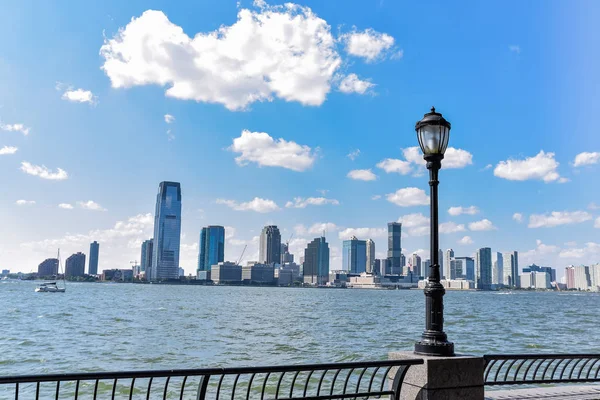 New Jersey skyline from Battery Park in a sunny day. Cityscape view through trees and streetlamp. City and travel concept. Manhattan, New York City, USA