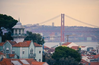 Lizbon panoramik manzarası. Lizbon binalarının renkli duvarları, turuncu çatıları ve arka planda 25 Nisan köprüsü, günbatımında. Seyahat ve emlak kavramı. Lizbon, Portekiz. Avrupa.