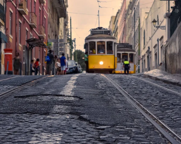 Travel concept of Lisbon's famous trams. Focusing on the cobbled streets with the trams in the foreground. In the background, tourists and trams out of focus, in the light of the sunset. Lisbon, Portu — Stock Photo, Image