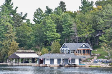 Gündüz vakti gölün kıyısındaki çimenli bir alanda ağaçlarla çevrili bir sürü farklı bina var. Gayrimenkul kavramı. Binlerce Adalar. Ontario, Kanada.